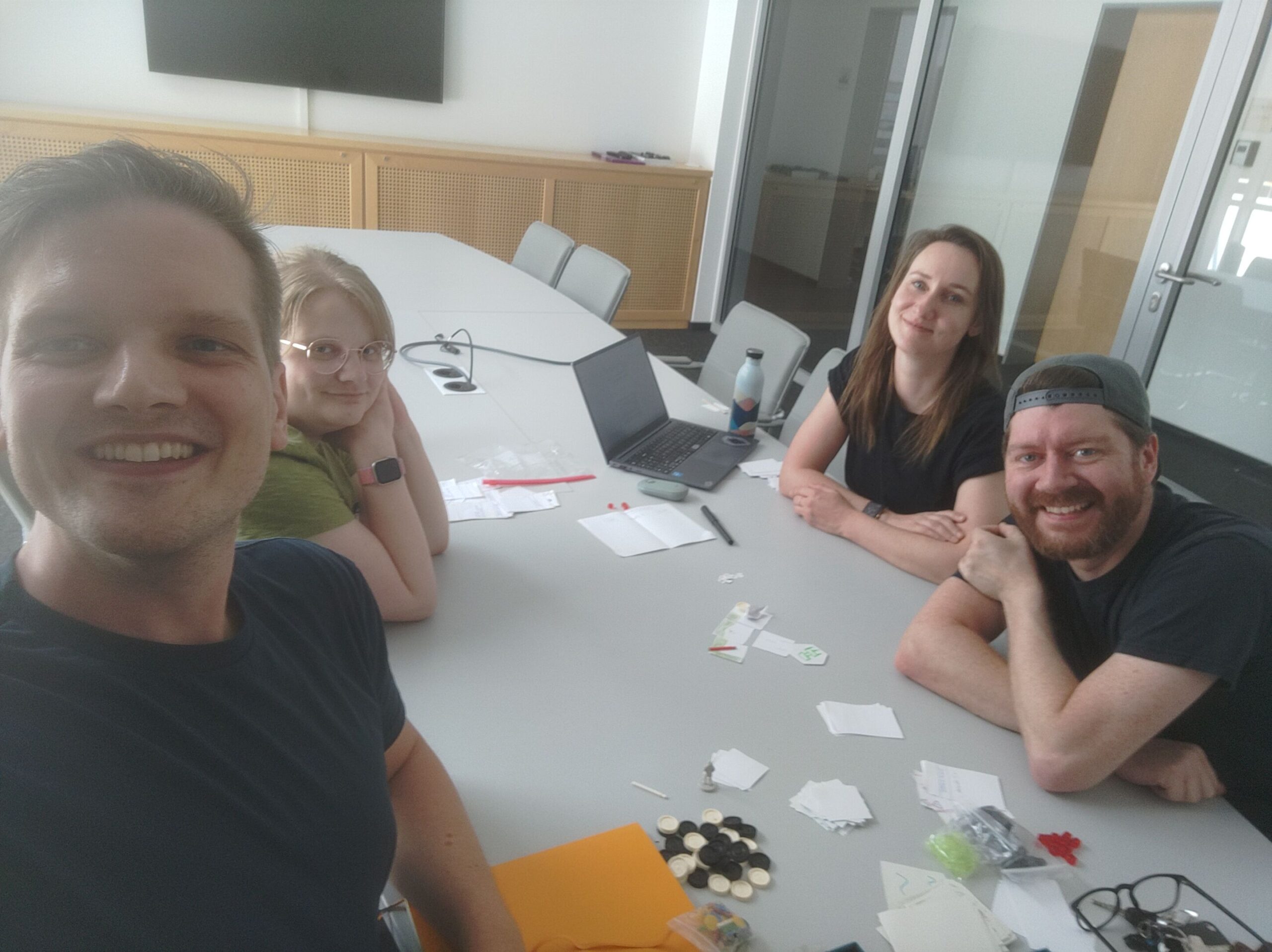 Four people smiling around a table during a collaborative SkillSaga game development workshop.