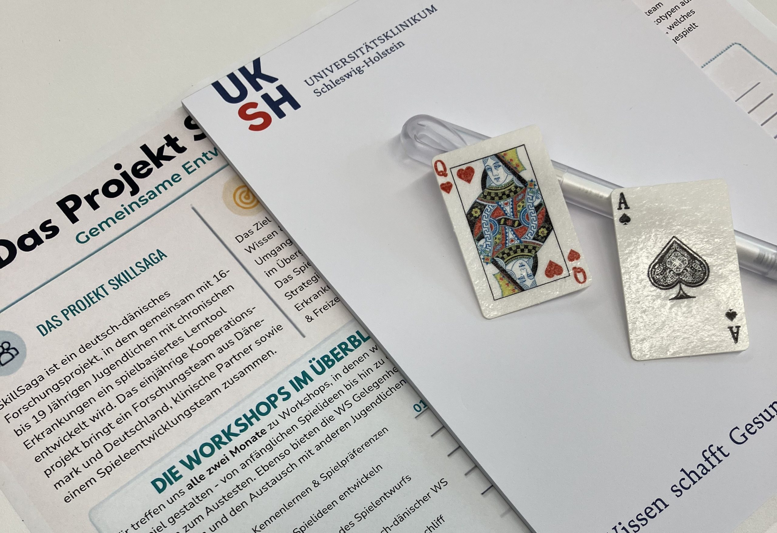 SkillSaga project brochure with workshop information beside playing cards and University Hospital Schleswig-Holstein branding.